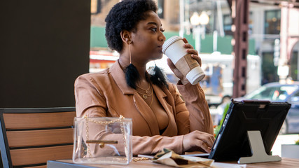 African american black woman enjoying dark coffee and brownies outdoors at a local cafe in Chicago downtown area during a beauty day outside. she is using her tablet to take care of business.