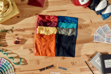 Workspace for Designer. Top view of neatly folded custom t shirts and arranged baseball caps....