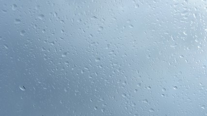 Close up view of water drops falling on glass. Rain running down on window.