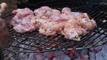 Man's hand putting a chicken meat with tongs to the charcoal barbecue grill.