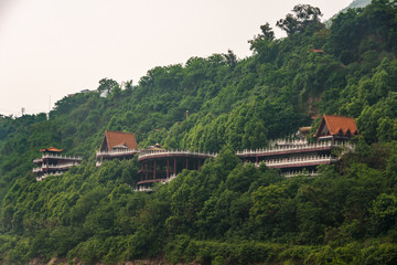 Fototapeta na wymiar Fengdu, Chongqing, China - May 8, 2010: Yangtze River. Classic architecture style red roofs popping above green forest on hill slope at large monstery. Some silver sky.