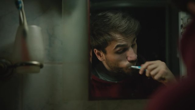 Reflection of young handsome bearded man is brushing teeth in the bathroom.