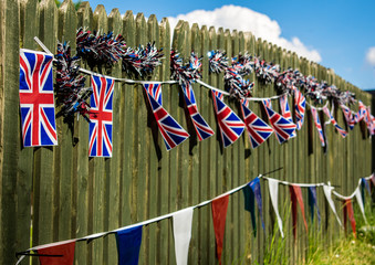 Union Jack bunting on a fence row, many flags in row on a string, triangular flags, front of garden VE day decorations in UK, memorial symbol of winning second world war