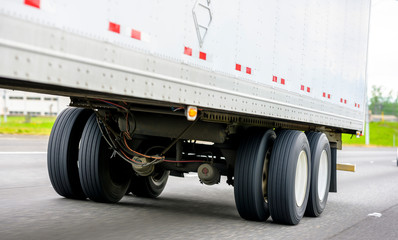 Fototapeta na wymiar Dual wheels trailer axles on the running on the road dry van semi trailer with cargo