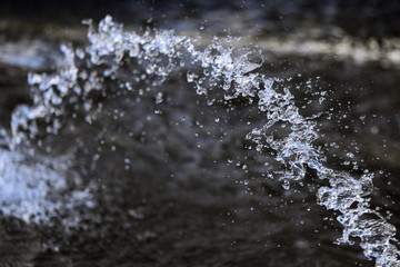 Water splashing from the fountain, jet, aqua drops, clear liquid splash on dark background