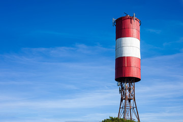 Red and white striped water tower against blue sky. 