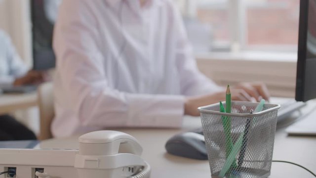 Lockdown of unrecognizable office worker wearing white shirt sitting at workplace, typing on computer keyboard and then answering telephone call