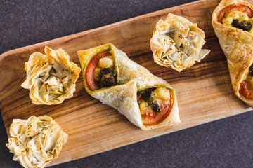 plant-based food, filo pastry cups and puff pastry envelopes with vegan cheese pesto and tomato filling on cutting board