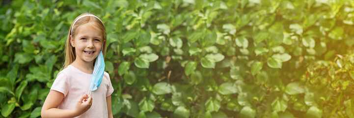 Happy little girl takes off protective medical mask from face outdoors. Web banner with copy space. Victory over coronavirus. The end of COVID-19 Pandemic crisis and lockdown