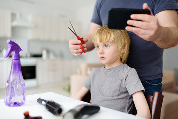 Preschooler boy gets haircut at home during quarantine. Hair cutting for kids by parents while barbershops closed.