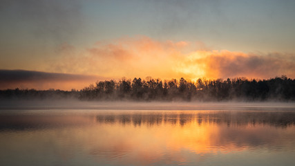 Sunrise on a foggy morning featuring a tree line at Lake Ontelaunee in Pennsylvania - obrazy, fototapety, plakaty