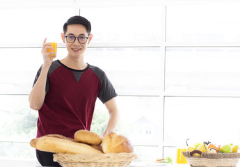 Young man holding glass orange juice while having tasty breakfast at the kitchen table, healthy concept.