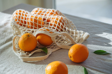 Mesh shopping bag with oranges on the table in sunset light with long shadow. concept of eco friendly social environmental responsibility. using zero waste eco reusable bag