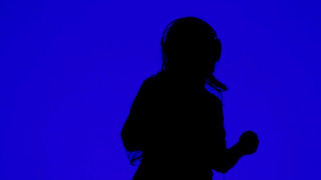 Silhouette of a woman in headphones and dancing to the music on a blue background