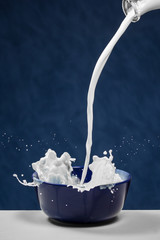 Milk pouring out of bottle and splashing in a bowl