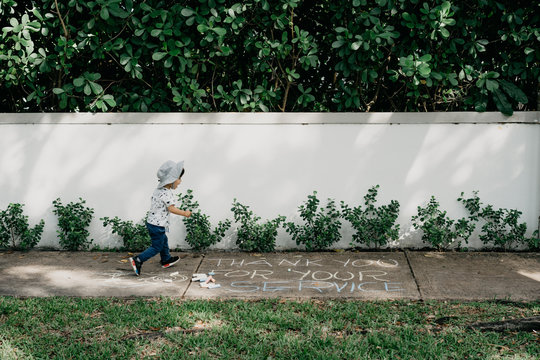 Toddler Running Through A Thank You For Your Service Sign On The Sidewalk