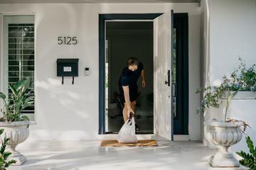 Man at home with a mask receiving food delivery