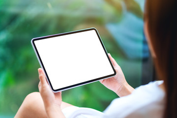 Mockup image of a woman holding black tablet pc with blank white desktop screen , green nature background