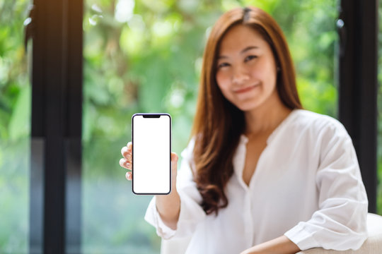 Mockup image of a beautiful asian woman holding and showing a mobile phone with blank white screen , blurred green nature background