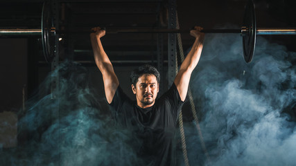 Obraz na płótnie Canvas asian strong athletic man having workout and bodybuilding with barbells weight over head squat setting style in gym and fitness club in dark tone