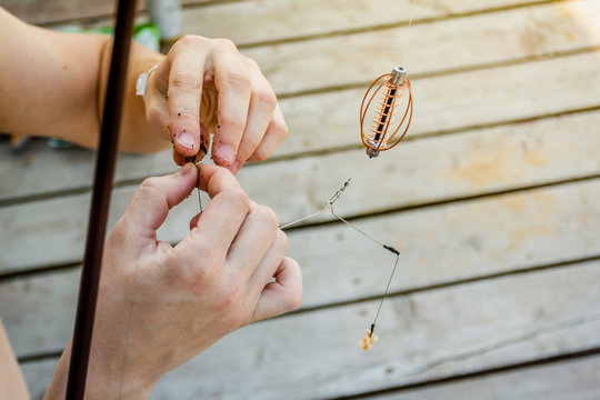 Close-up of the hands of a fisherman who impales worms on the hook of a fishing rod on a wooden pier.