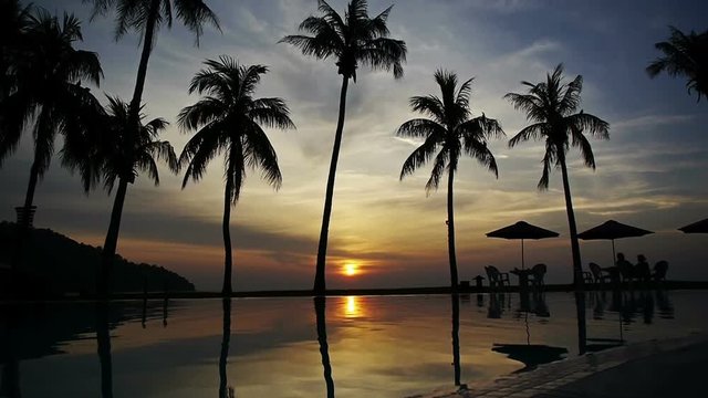 Sun setting reflected in pool water under the palm trees in a tropical resort 1 