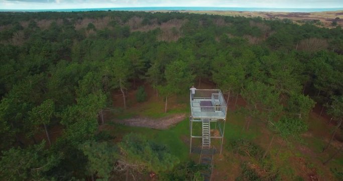 Young lonely boy or man standing on watchtower looking over the trees staring at the horizon and nature - tilt down and fly over reveal drone shot - 4k