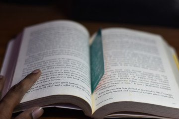 boy reading a book Think and grow rich, by Napoleon Hill, on the table with shallow depth of field 