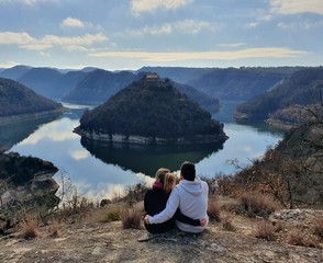 Una pareja sentada en el bosque mientras observa un río y su precioso paisaje.