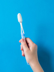 A child's hand with a blue toothbrush on a blue background.