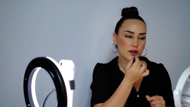 Attractive beauty blogger making online broadcast to her subscribers about makeup with phone in front of ring light, slow motion shooting beauty influencer vlog.