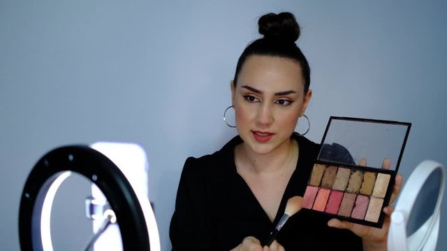 Attractive beauty blogger making online broadcast to her subscribers about makeup with phone in front of ring light, slow motion shooting beauty influencer vlog.