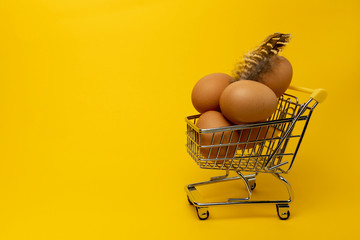 Еggs. Five brown eggs in a mini supermarket trolley and feather on an orange background close-up....