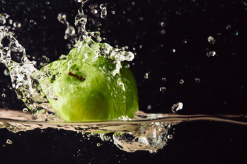 Green apple falling in water with splash on black background.