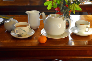 A set of hot tea, teapot, tea cups on mug, milk jar and an orange fruit wooden table in afternoon. Traditional english tea.