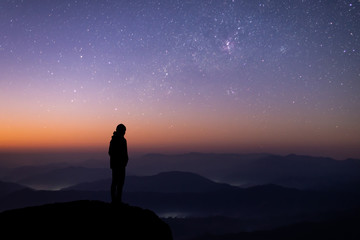 Fototapeta premium Silhouette of young traveler watched the star and milky way on top of the mountain alone before sunrise. He is happy to be with herself and stay with nature at twilight time.