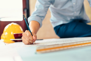 engineers holding a pen pointing to a building and  drawing outlay construction plan as guide for...