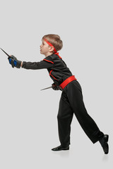 Young boy in ninja uniform practicing knife throwing on light gray background