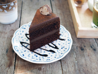 A piece of chocolate fudge cake; decorated with cocoa powder, wafer and chocolate sauce served on white plate over wooden board. Selective focus.
