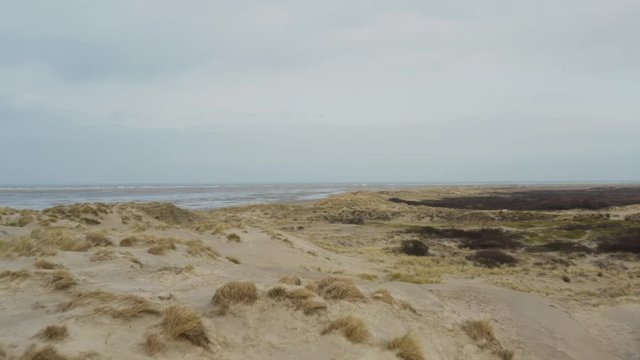 Drone aerial shot over windy frisian island Borkum dunes revealing north sea, empty beach and wadden sea in the background.