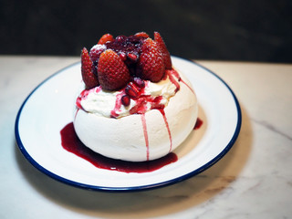 Summer Berry Pavlova, Meringue pavlova filled with fresh cream, fresh strawberry and pomegranate, served with juicy berry sauce on white plate. Selective focus.