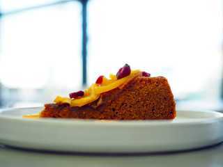 A delicious sliced of organic flourless cake decorated with dried cranberry and orange on white plate. Healthy and vegan concept. Selective focus with blur background.