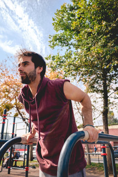 Handsome young man portrait training calisthenics with arms with muscles on parallel bars in a street workout park on a sunny day with nature and blue sky