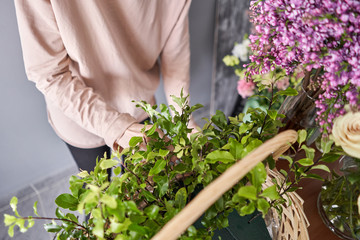A woman writes a video blog or online course. Flower school concept. Florist woman creates flower arrangement in a wicker basket. Flowers delivery.