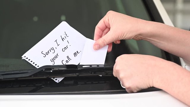 Woman car driver hands leaving a sorry I hit your car note on vehicle windshield