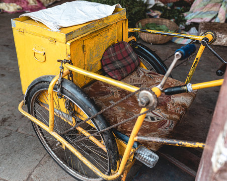 An isolated hand driven Handicapped tricycle of a poor person parked on the street side with no person on it. Yellow wheelchair of a disabled individual in the Indian city of Delhi.