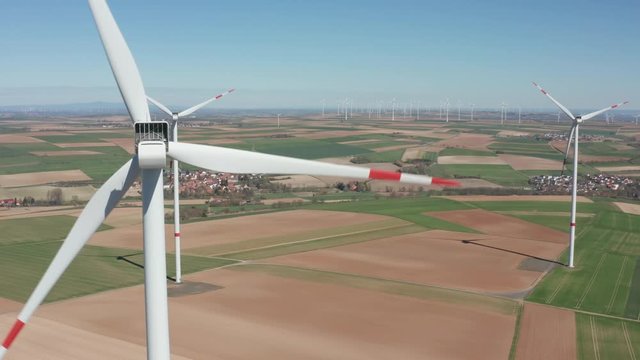 Rotating wings of  wind power plant producing renewable green clean engergy electricity in a wind farm on a sunny day, drone aerial cinematic rotating clops up shot, 25p