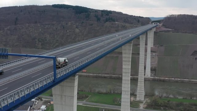 Hochmoselbr&uuml;cke High Moselle Bridge in Rhineland-Palatinate Germany with traffic cars and trucks on a freeway highway cinematic inflow medium aerial drone shot on a sunny cloudy day 25p