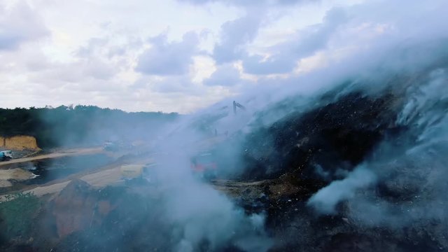 Aerial, drone shot through blue smoke, firetrucks and firefighters trying to calm down the and wildfire, cloudy evening, in the Amazon jungle, Brazil, South America
