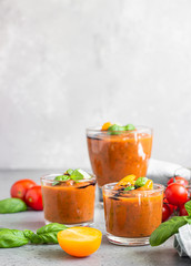 Delicious gazpacho soup in glass. Traditional spanish cold soup puree gaspacho garnish with tomato, cucumber and basil. Grey concrete background.